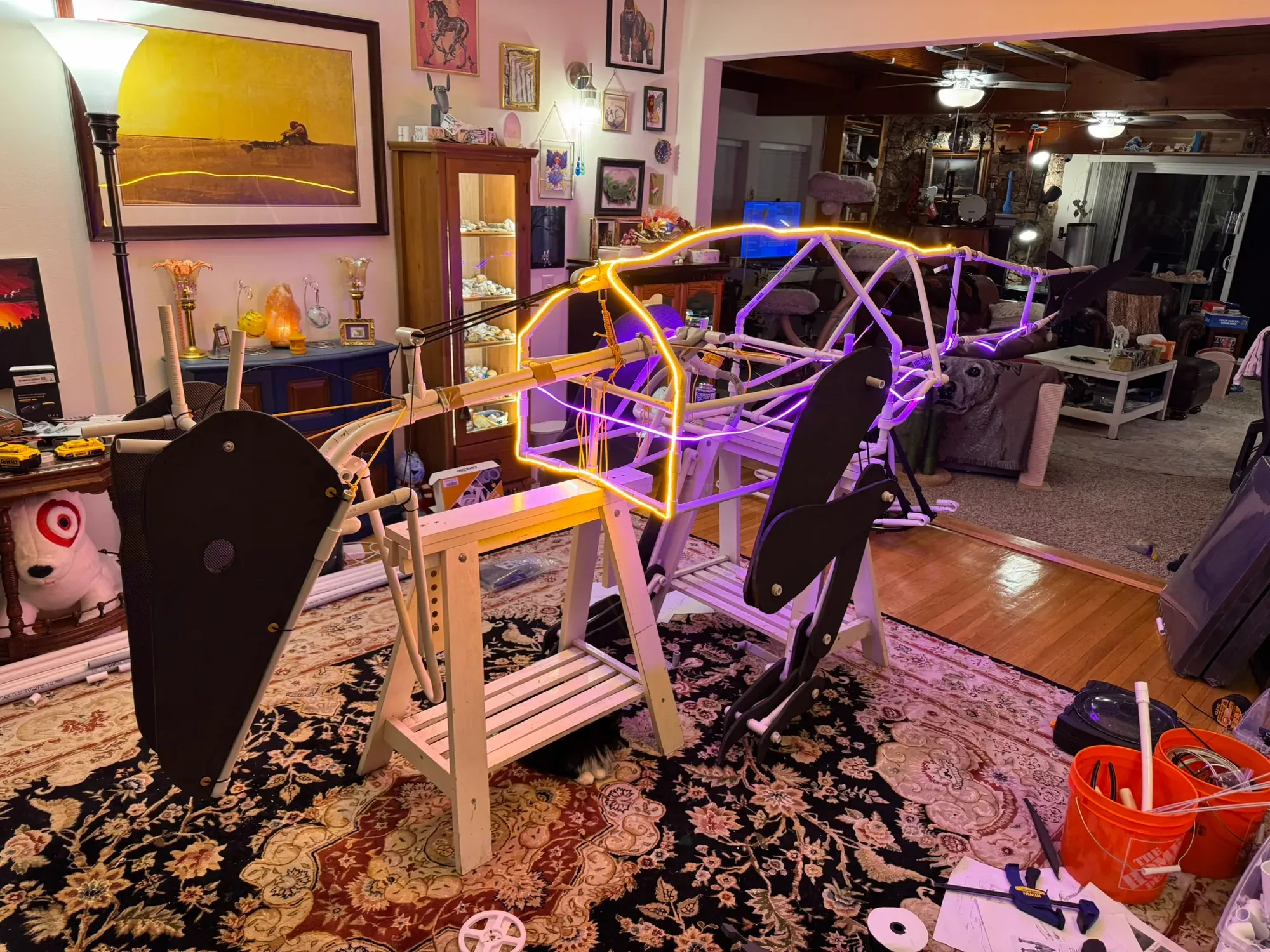 Night lighting test: orange and pink COB LED strips tracing the frame, dark foam plates mounted, the whole rig glowing on sawhorses