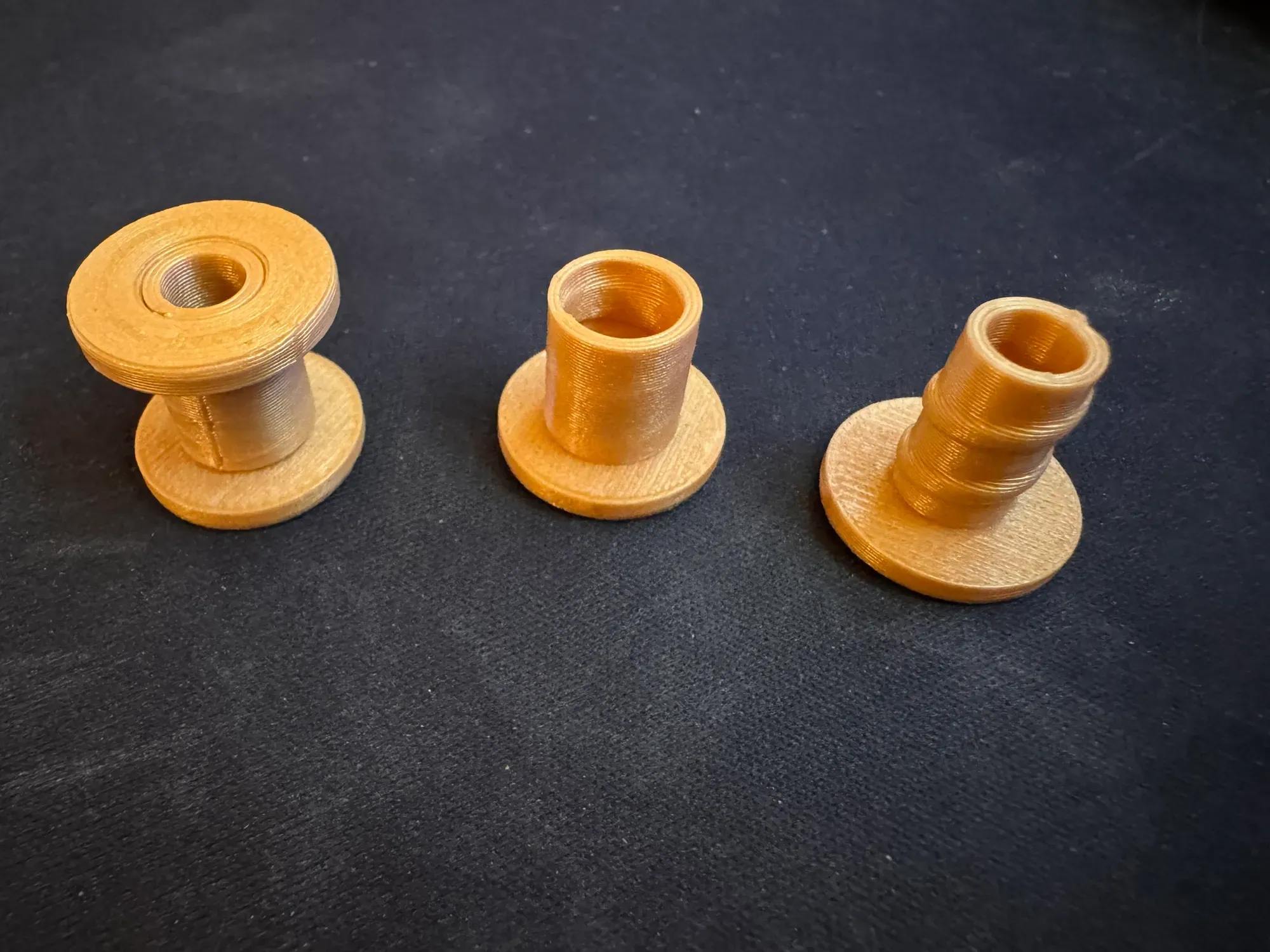 Three orange 3D-printed through-hull parts on dark foam: one assembled pair and the two halves, one smooth and one ridged