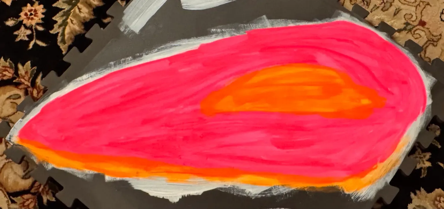The first foam body plate painted hot pink with an orange center, drying on a workshop mat